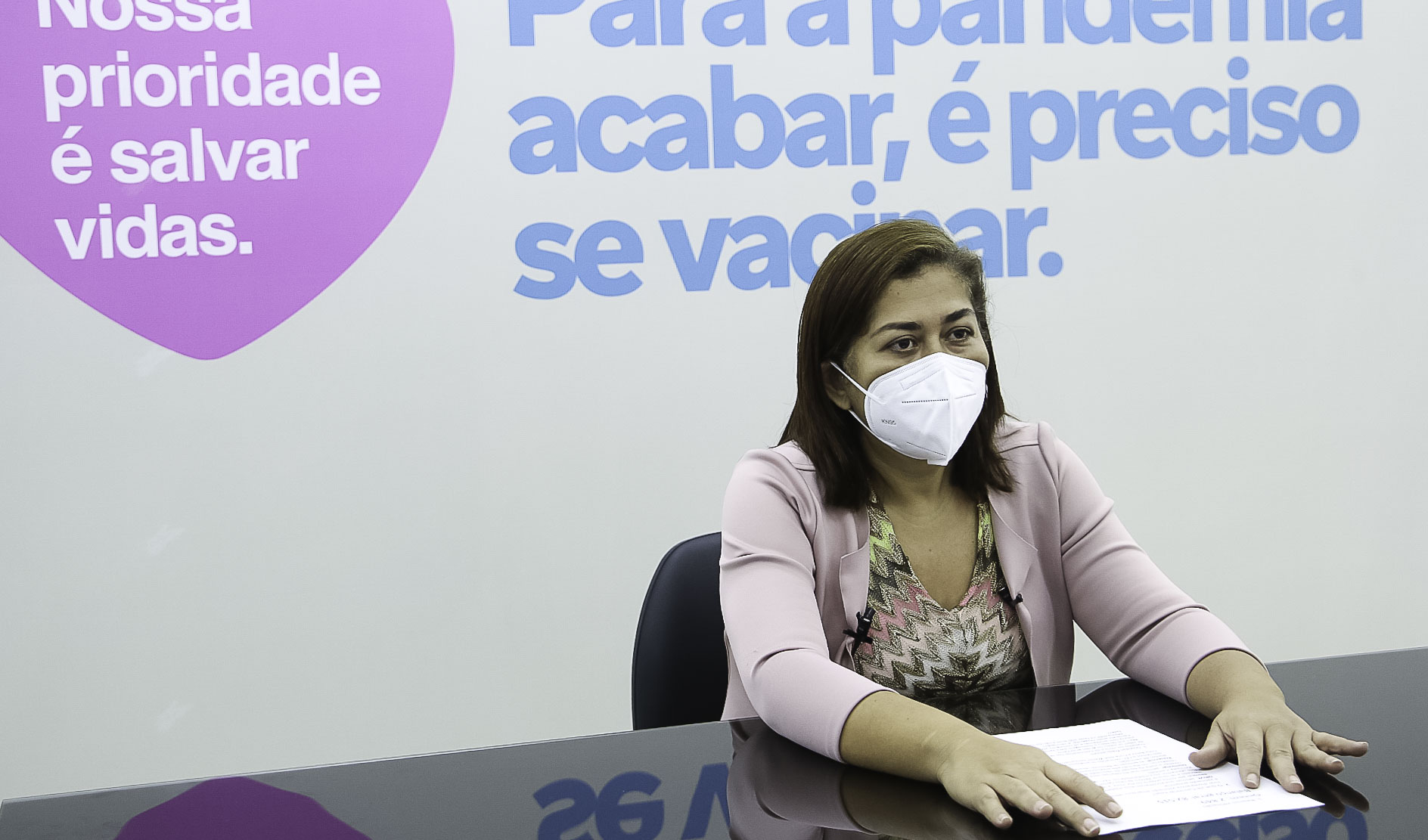 Fabiana Sales sentada diante de uma mesa enquanto grava a live